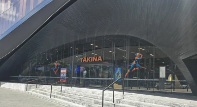 At the entrance of Tākina Convention Centre, concrete stairs lead up to a set of glass doors in a half circle frame adorned with captivating Marvel-themed attractions. 