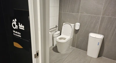 A toilet with wheelchair access has grey tiles and a black door. Whaikaha accessible appears on the door. 