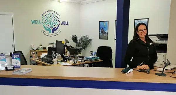  The WellABle office is brightly lit, with their logo prominently displayed in the center of the wall behind the computers. Maria, their information advisor, is doing an excellent job at the front desk.