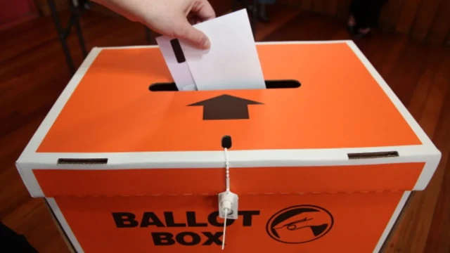 A hand dropping a voting paper into an orange ballot box