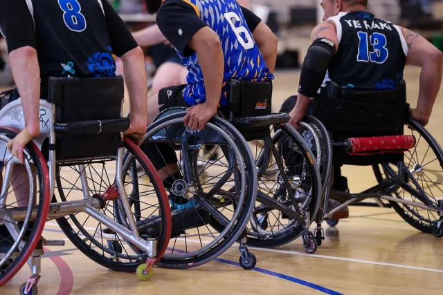 A low, behind view of three wheelchair basketball players, focusing on their chairs.