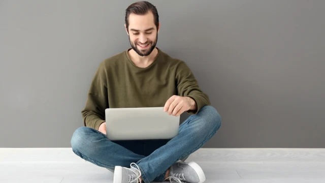 A man sitting on a floor using a laptop computer on his lap