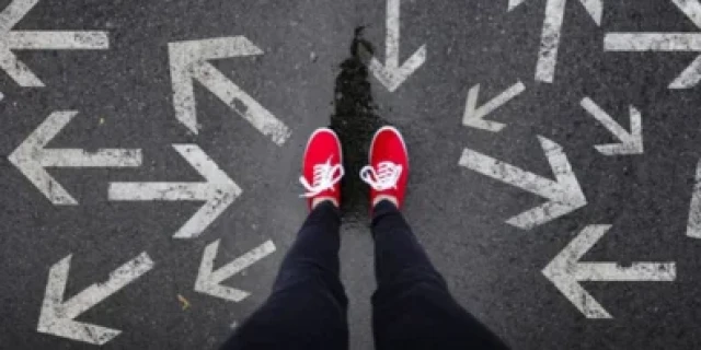 Someon's first person view of their feet, wearing red sneakers, surrounded by arrows on the ground pointing in different directions.