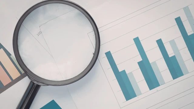 A magnifying glass on top of papers featuring graphs