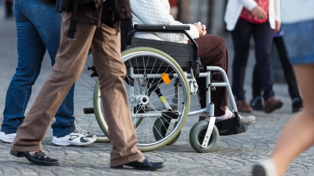 A person in a wheelchair being pushed along a crowded street. The shot is taken a waist height.