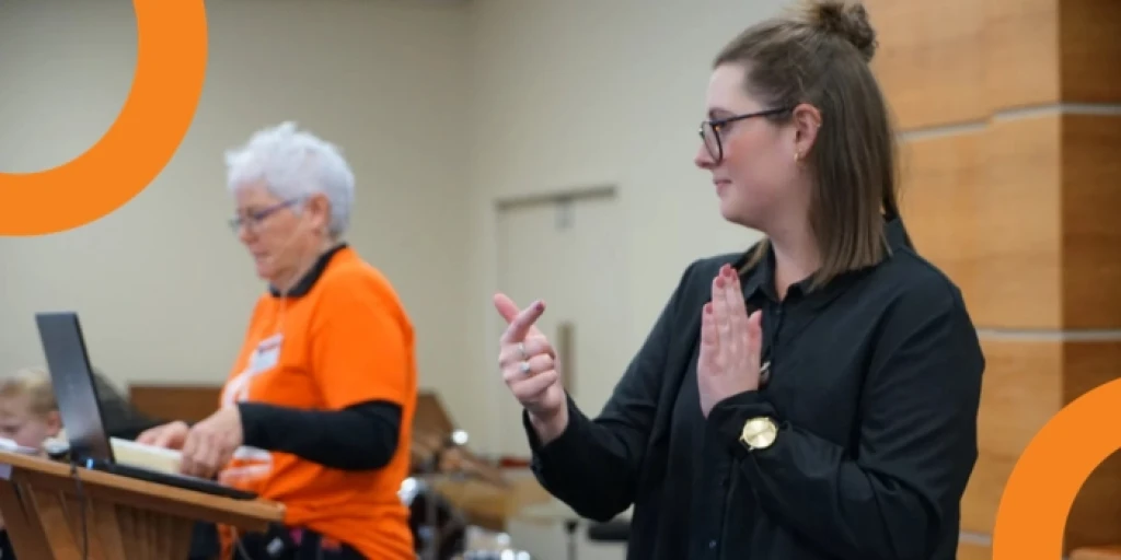 A woman doing New Zealand Sign Language next to another woman reading from a lecturn