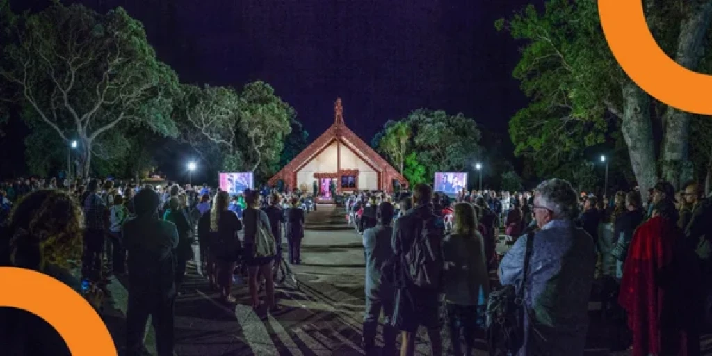 A group of people gathered outside a wharenui at Waitangi.