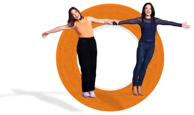 Molly and Kate, two women of European and Māori descent, lean outward while holding hands, maintaining a strong connection despite their opposing balance.