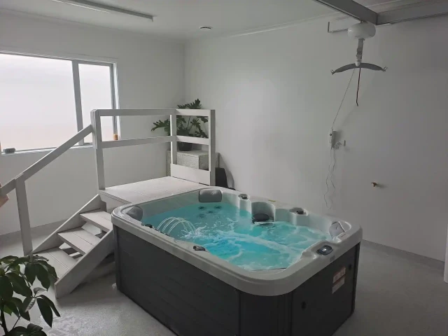 Spa pool with wooden steps to the side and a hoist suspended from the ceiling above