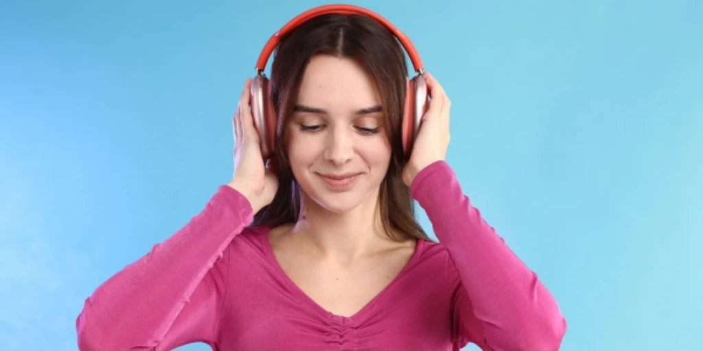 A woman in a pink shirt listening to a pair of red headphones.