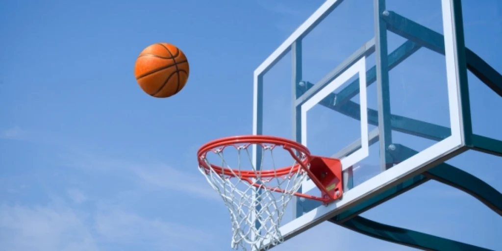 A basketball flying through the air towards an outdoor basketball hoop.