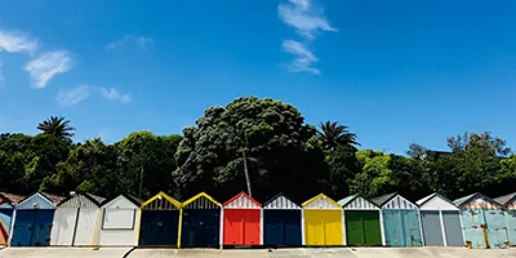 A row of different coloured sheds in front of some green trees