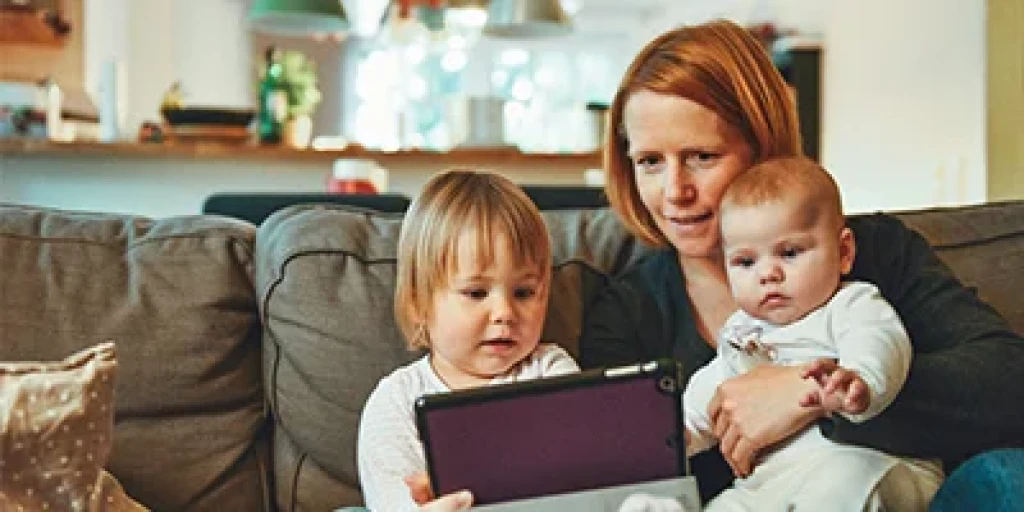 A woman sitting on the couch with her two young children looking at a tablet