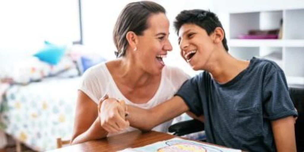 Woman and young man sitting at a table holding hands and laughing.