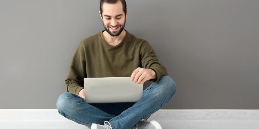 A man sitting on a floor using a laptop computer on his lap