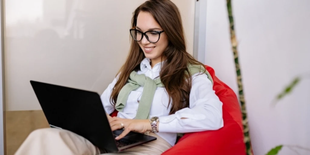 A woman sitting on a beanbag with a laptop computer on her lap.