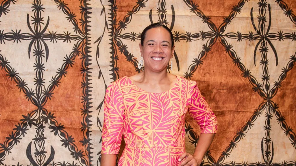 A Pasifika woman standing in front of traditional designs