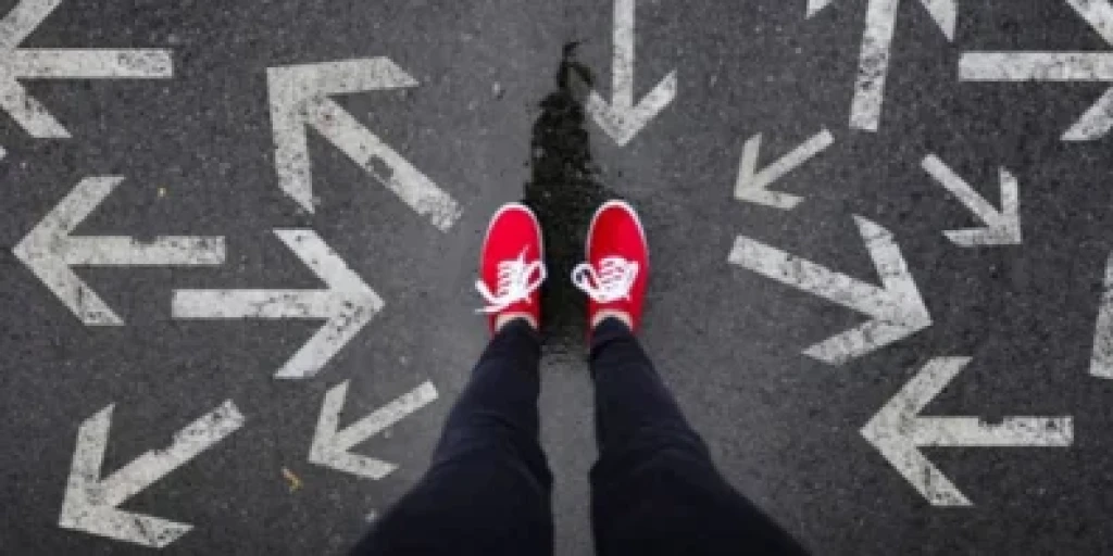 Someon's first person view of their feet, wearing red sneakers, surrounded by arrows on the ground pointing in different directions.