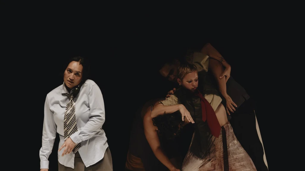 Three people doing a dance performance in front of a black background