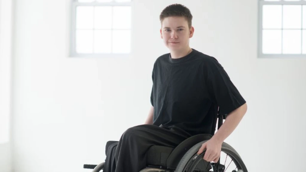 Teen boy wearing all black in a wheelchair in a white room