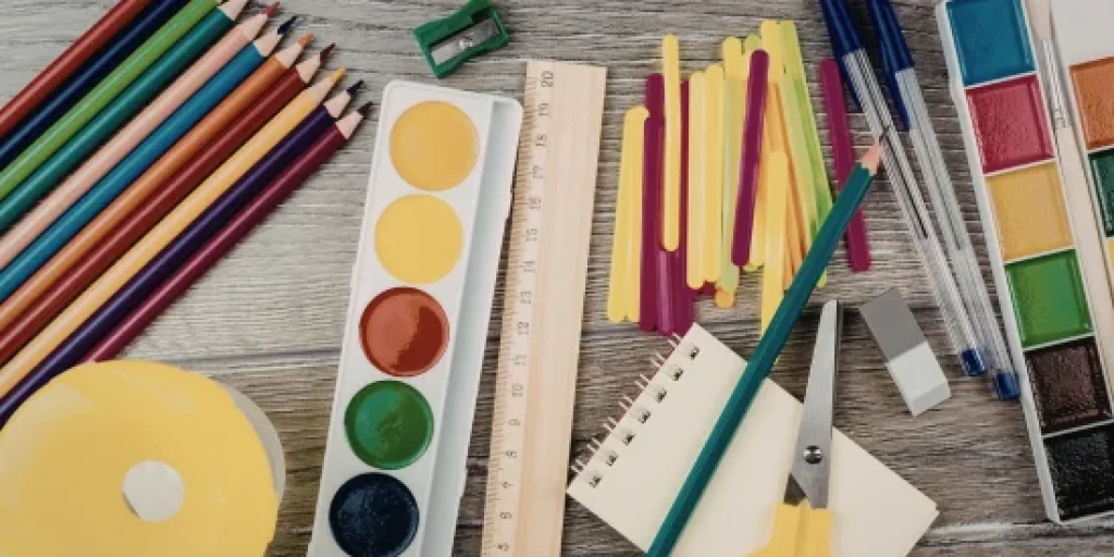 Art supplies spread across a table, including pencils, paints, paper, a pair of scissors and a ruler.