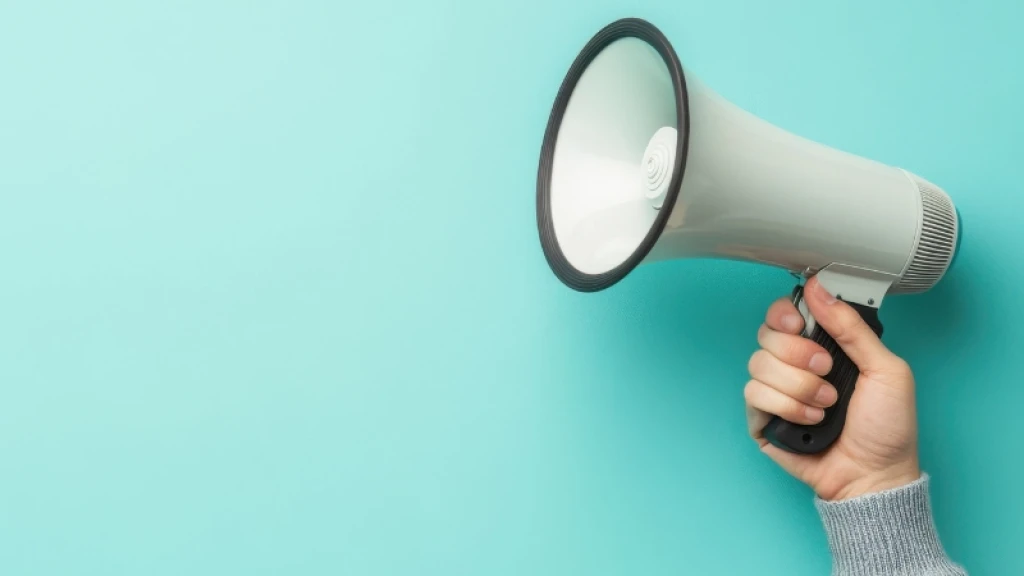 A hand holding a white megaphone in front of a green background
