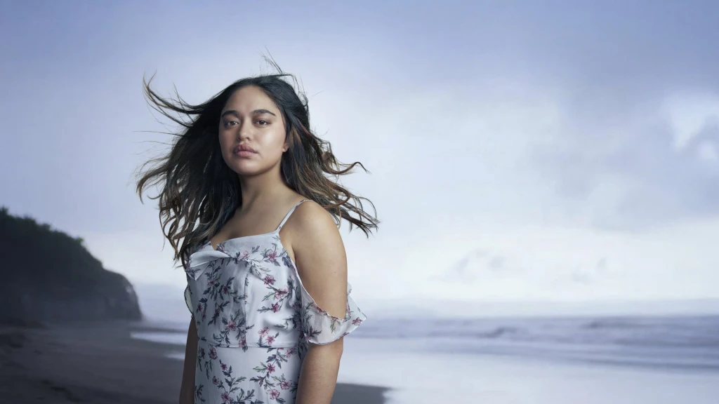 A woman standing on beach with a grey sky and the ocean behind her