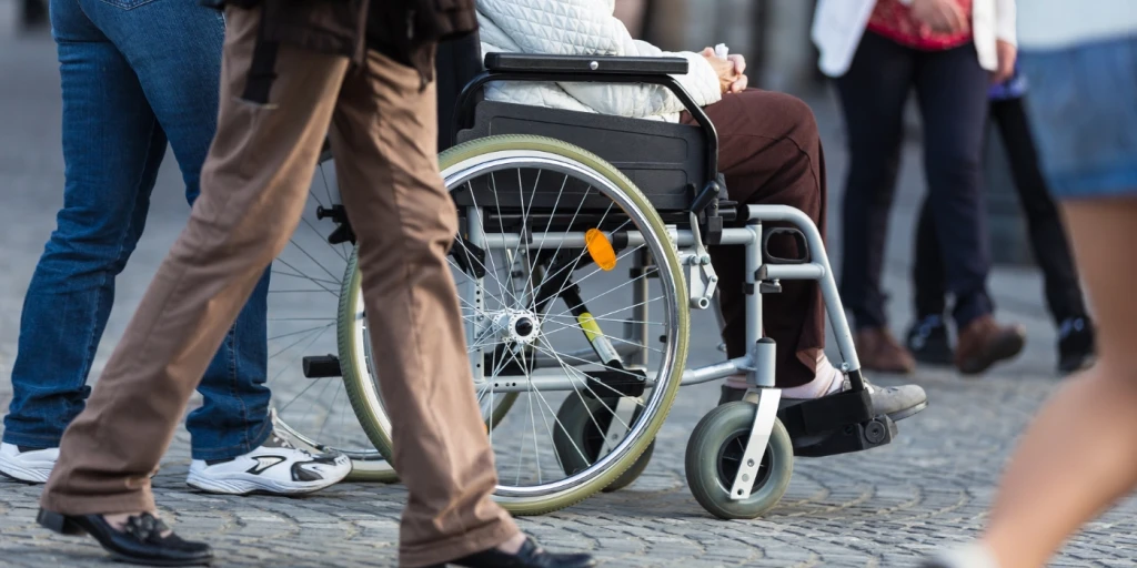 A person in a wheelchair being pushed along a crowded street. The shot is taken a waist height.