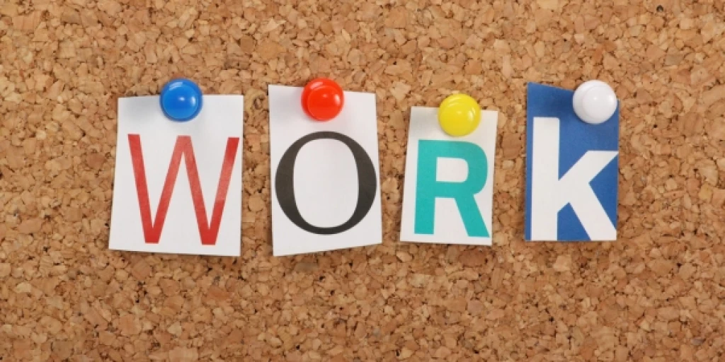 Pieces of paper each with a letter spelling out the word 'Work' pinned to a cork board.